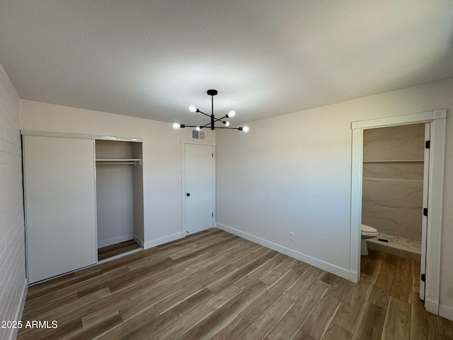 unfurnished bedroom with a closet, baseboards, an inviting chandelier, visible vents, and wood finished floors