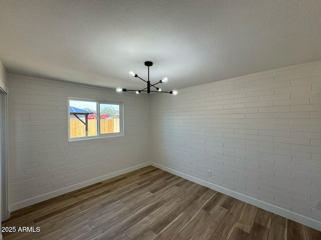 spare room with brick wall, an inviting chandelier, baseboards, and dark wood finished floors