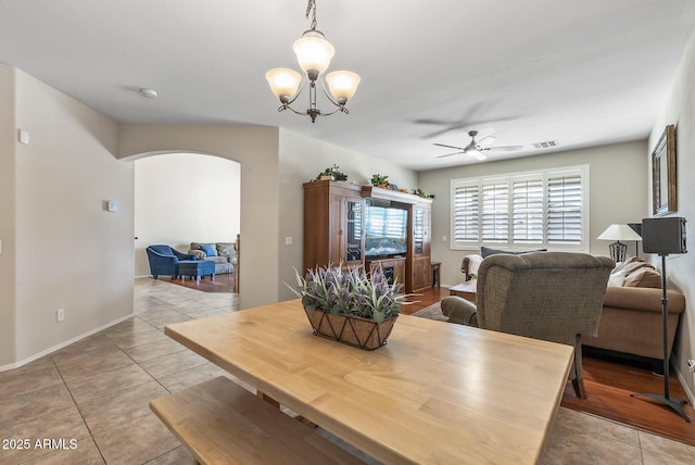 dining area with ceiling fan with notable chandelier, light tile patterned floors, visible vents, and arched walkways