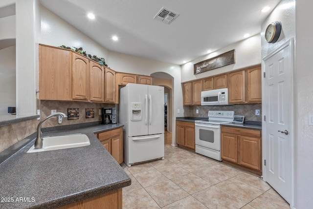 kitchen featuring visible vents, a sink, dark countertops, white appliances, and arched walkways