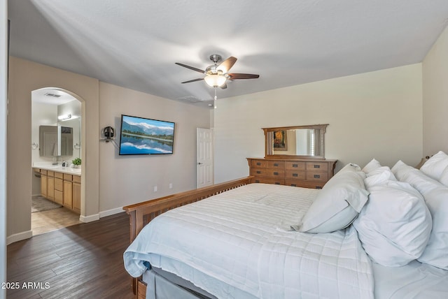 bedroom with wood finished floors, visible vents, baseboards, ensuite bath, and arched walkways