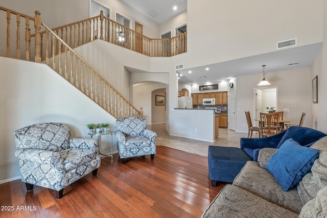 living room with stairs, light wood-style floors, visible vents, and arched walkways