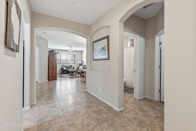 hall featuring light tile patterned floors, visible vents, baseboards, and arched walkways