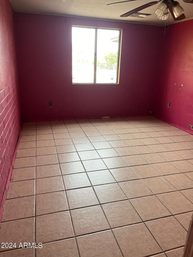 tiled empty room with ceiling fan and brick wall