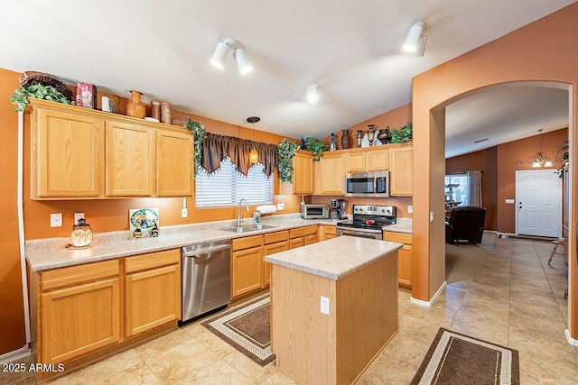 kitchen with a sink, stainless steel appliances, arched walkways, light countertops, and lofted ceiling