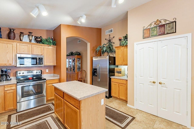 kitchen featuring visible vents, a center island, arched walkways, appliances with stainless steel finishes, and light countertops