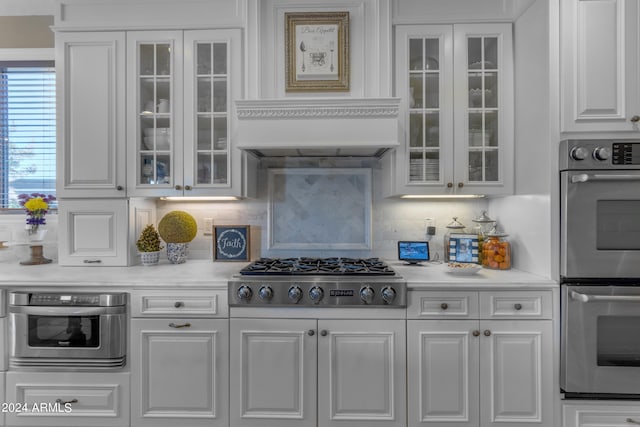 kitchen with decorative backsplash, white cabinets, appliances with stainless steel finishes, and premium range hood