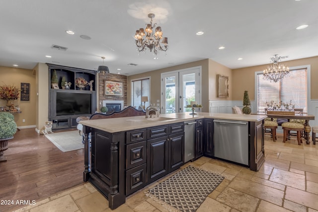 kitchen featuring a center island with sink, sink, a fireplace, hanging light fixtures, and stainless steel dishwasher