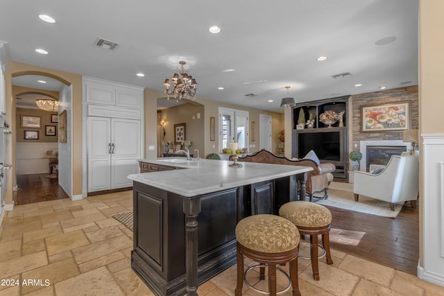 kitchen featuring a large fireplace, light stone countertops, hanging light fixtures, white cabinets, and a spacious island