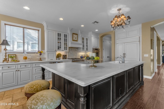 kitchen with white cabinets, an island with sink, sink, stainless steel oven, and decorative backsplash