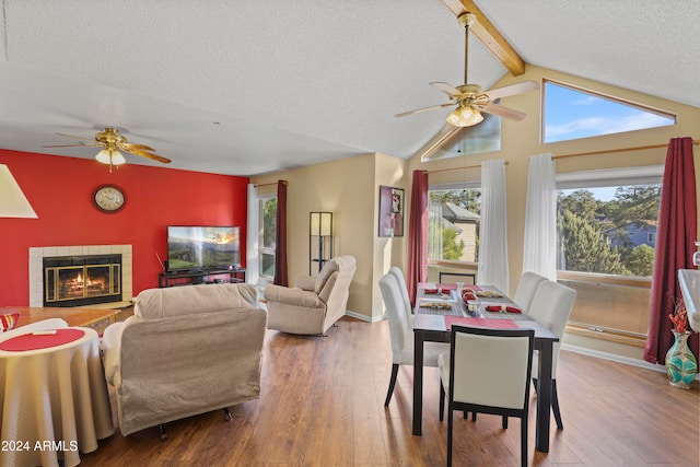 dining room featuring a fireplace, hardwood / wood-style floors, lofted ceiling with beams, and a textured ceiling