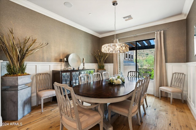 dining space featuring a wainscoted wall, a notable chandelier, visible vents, ornamental molding, and light wood-type flooring