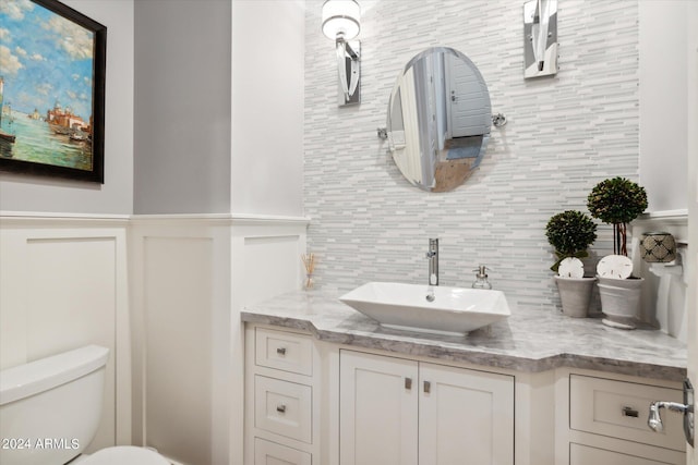 bathroom featuring tasteful backsplash, a wainscoted wall, vanity, and toilet