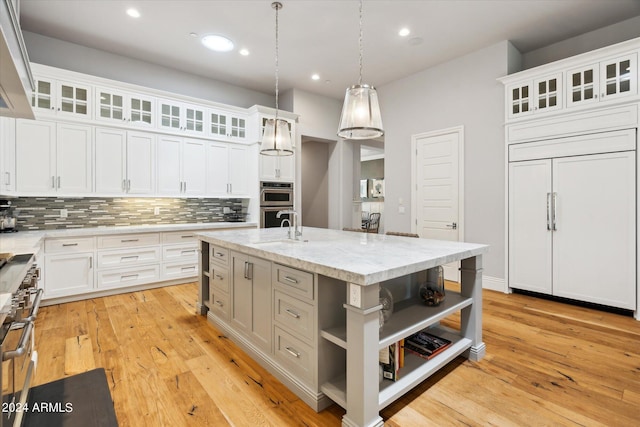 kitchen featuring white cabinets, decorative light fixtures, tasteful backsplash, and an island with sink