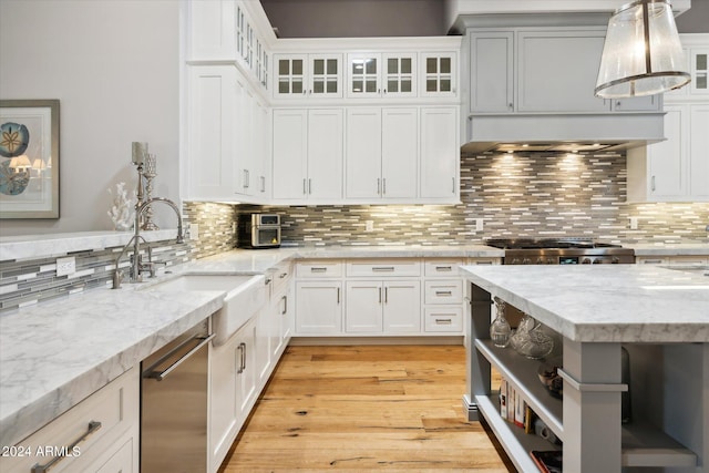 kitchen with tasteful backsplash, dishwasher, light wood-style flooring, light stone counters, and a sink