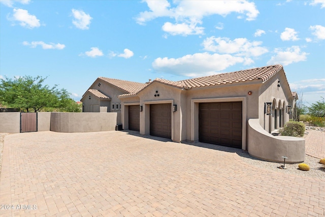 mediterranean / spanish-style home featuring decorative driveway, stucco siding, an attached garage, fence, and a tiled roof