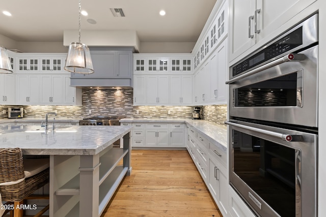 kitchen featuring light wood finished floors, tasteful backsplash, visible vents, double oven, and pendant lighting