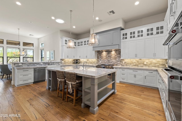 kitchen featuring stainless steel dishwasher, stove, backsplash, and an island with sink