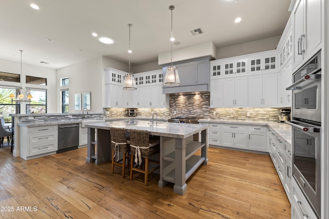 kitchen with light wood finished floors, stainless steel appliances, visible vents, decorative backsplash, and a kitchen island with sink