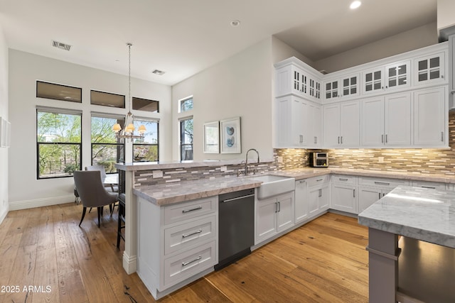 kitchen featuring visible vents, backsplash, a sink, a peninsula, and dishwashing machine