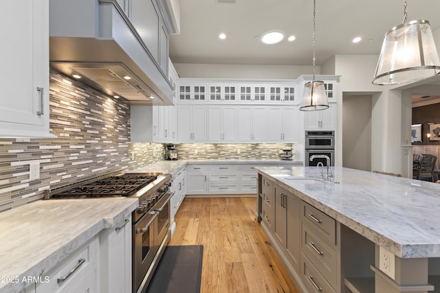 kitchen featuring a sink, wall chimney range hood, appliances with stainless steel finishes, light wood-type flooring, and backsplash