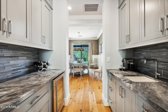 kitchen featuring visible vents, wine cooler, dark stone countertops, light wood-type flooring, and a sink