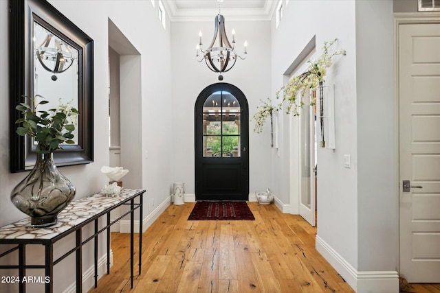 entrance foyer featuring arched walkways, baseboards, light wood finished floors, and an inviting chandelier