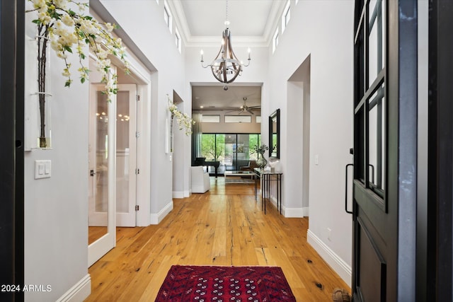 entryway featuring light wood-style flooring, baseboards, crown molding, and ceiling fan with notable chandelier