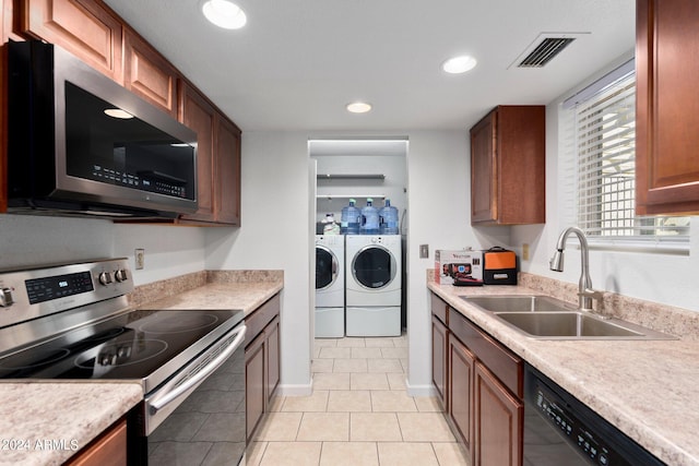 kitchen with appliances with stainless steel finishes, washer and dryer, sink, and light tile patterned floors