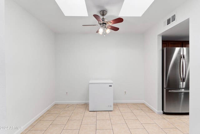 tiled empty room featuring ceiling fan and a skylight