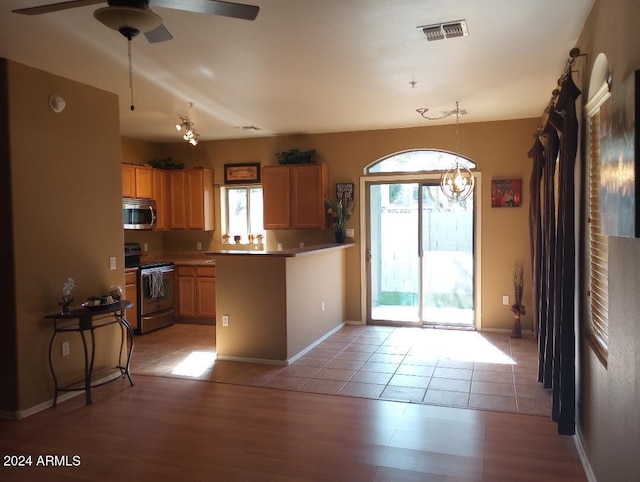 kitchen featuring kitchen peninsula, appliances with stainless steel finishes, light wood-type flooring, ceiling fan with notable chandelier, and decorative light fixtures