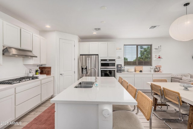 kitchen with a sink, stainless steel appliances, under cabinet range hood, an island with sink, and white cabinets