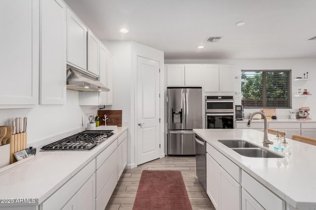 kitchen with stainless steel appliances, a sink, under cabinet range hood, white cabinetry, and recessed lighting