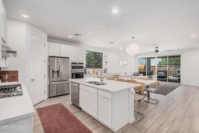 kitchen featuring stainless steel appliances, a sink, light wood finished floors, white cabinetry, and light countertops