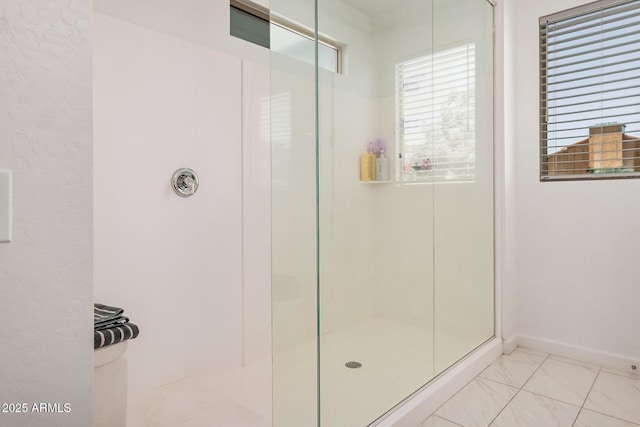 bathroom with a shower with door, marble finish flooring, and baseboards