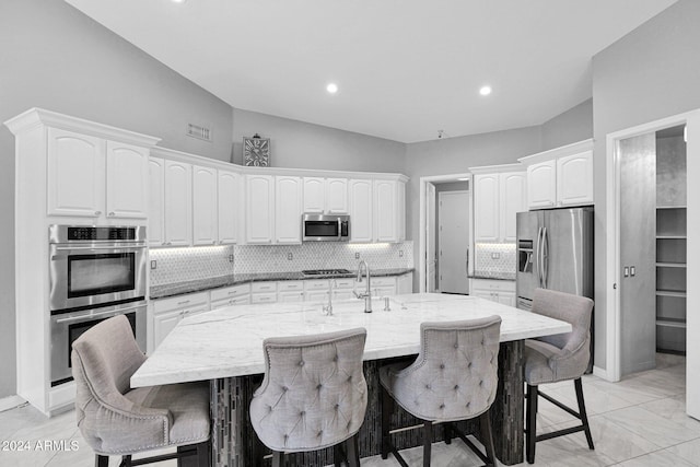 kitchen with a kitchen bar, appliances with stainless steel finishes, white cabinetry, and a kitchen island with sink