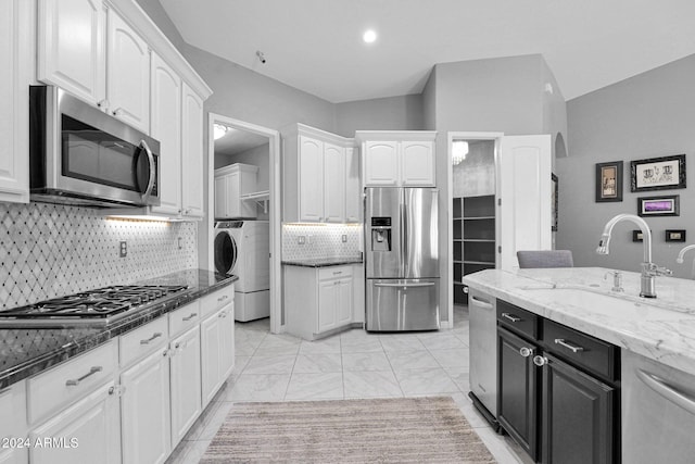 kitchen featuring sink, dark stone counters, washer / dryer, white cabinets, and appliances with stainless steel finishes