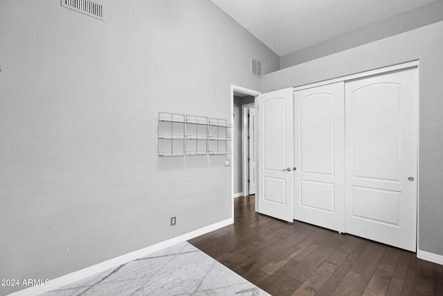 unfurnished bedroom featuring dark hardwood / wood-style flooring, vaulted ceiling, and a closet