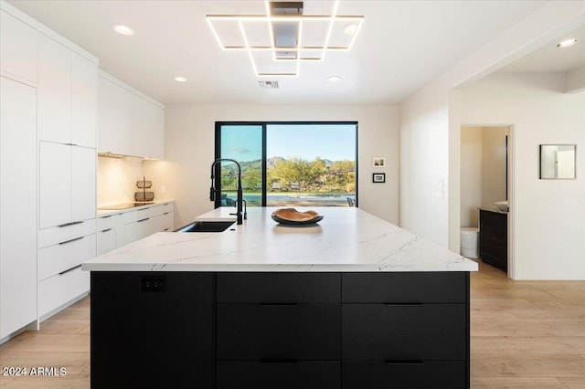 kitchen featuring light wood-type flooring, a center island with sink, sink, and white cabinetry