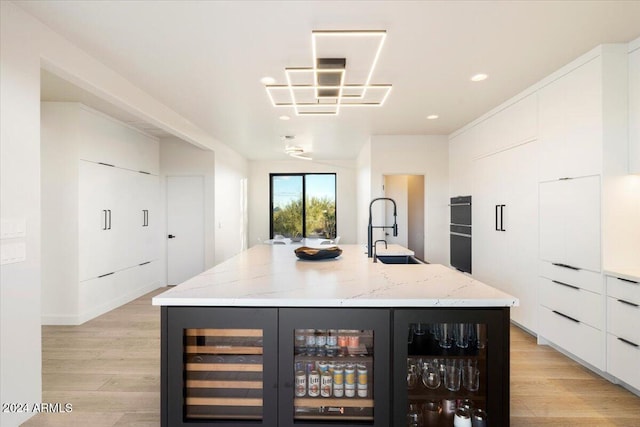 interior space with light wood-type flooring, sink, light stone counters, and white cabinets