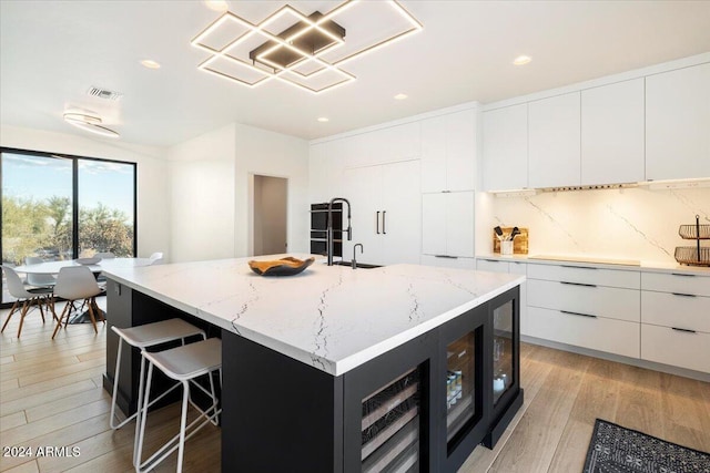 kitchen featuring light hardwood / wood-style floors, a center island with sink, light stone counters, sink, and white cabinetry