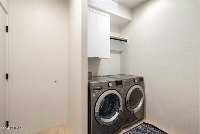 clothes washing area with hardwood / wood-style floors, washer and dryer, and cabinets