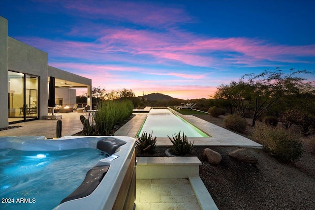 pool at dusk with a patio and a hot tub