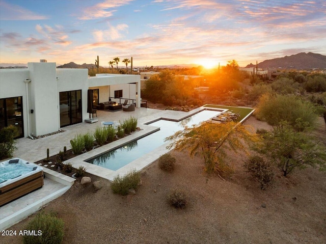 back house at dusk featuring a mountain view, a patio, and a swimming pool with hot tub