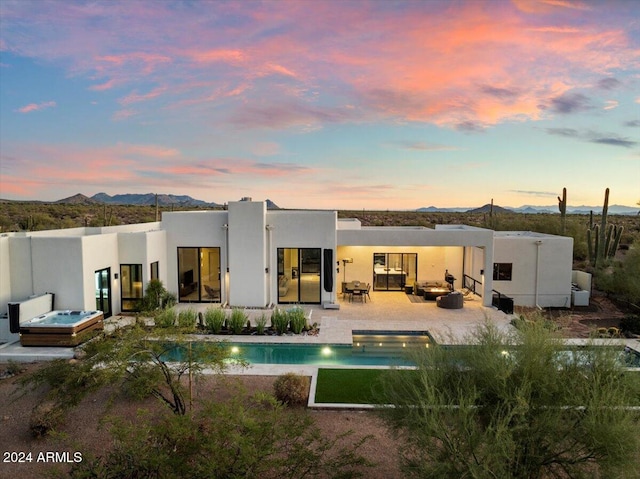 back house at dusk with a pool with hot tub, a patio, a mountain view, and an outdoor hangout area