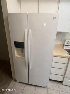 interior details with stove, light countertops, white cabinetry, and white refrigerator with ice dispenser