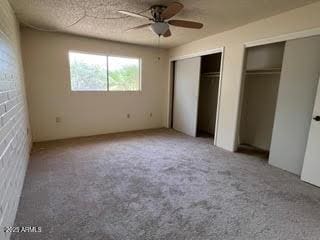 unfurnished bedroom with carpet flooring, a ceiling fan, and multiple closets