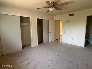 unfurnished bedroom featuring visible vents, ceiling fan, multiple closets, and ensuite bathroom