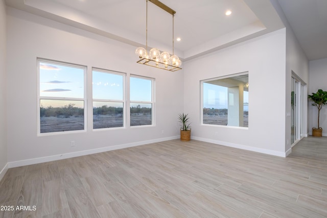 spare room featuring light hardwood / wood-style floors, a raised ceiling, and a chandelier