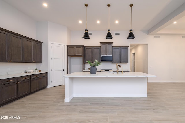 kitchen featuring a kitchen island with sink, dark brown cabinets, and decorative light fixtures